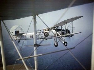 Close-up of a Fairey Swordfish Mark II, HS 545'B', in flight as seen through the struts of another aircraft.